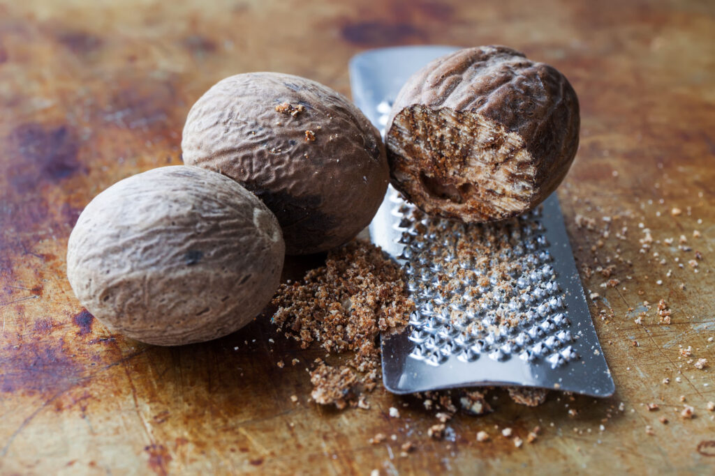 Making nutmeg powder process. Nuts silver grater. Kitchen still life photo. Shallow depth of field, aged brown rusty background. Selective focus.